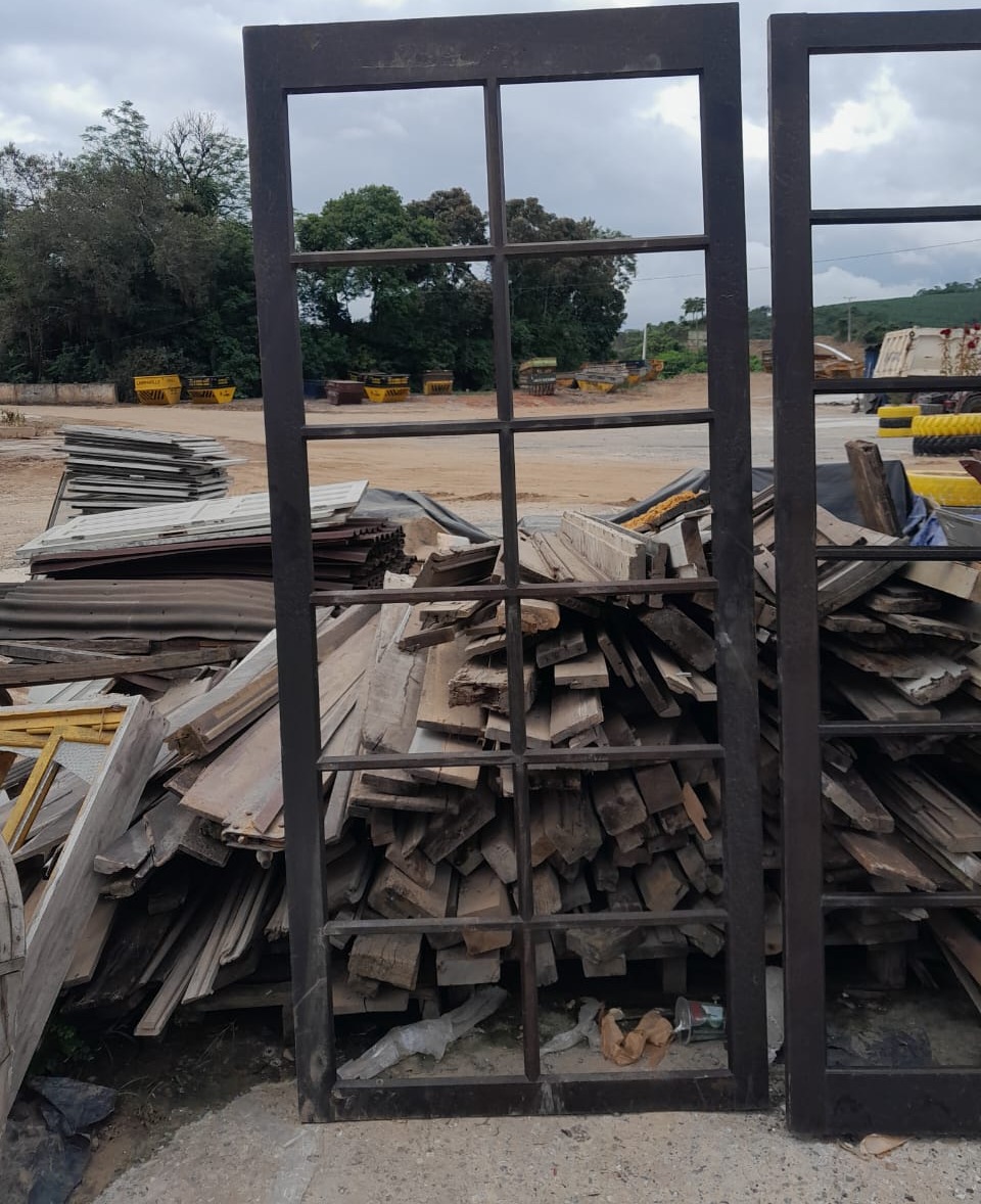 Pátio com pilhas de madeira reaproveitada e esquadrias metálicas reaproveitadas disponíveis para venda.