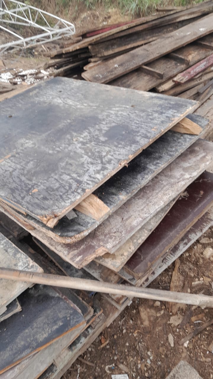 Pilha de chapas de compensado e tábuas de madeira reutilizadas no pátio da empresa, mostrando o estoque real de material de construção civil reaproveitado.