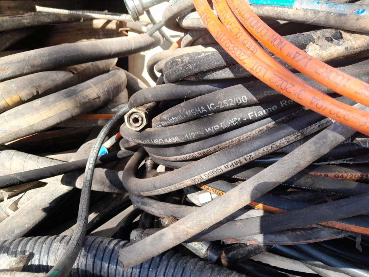 Pilha de mangueiras hidráulicas industriais reutilizadas, com especificações de pressão (3000 PSI) e resistência a chama, ilustrando o estoque de materiais reap