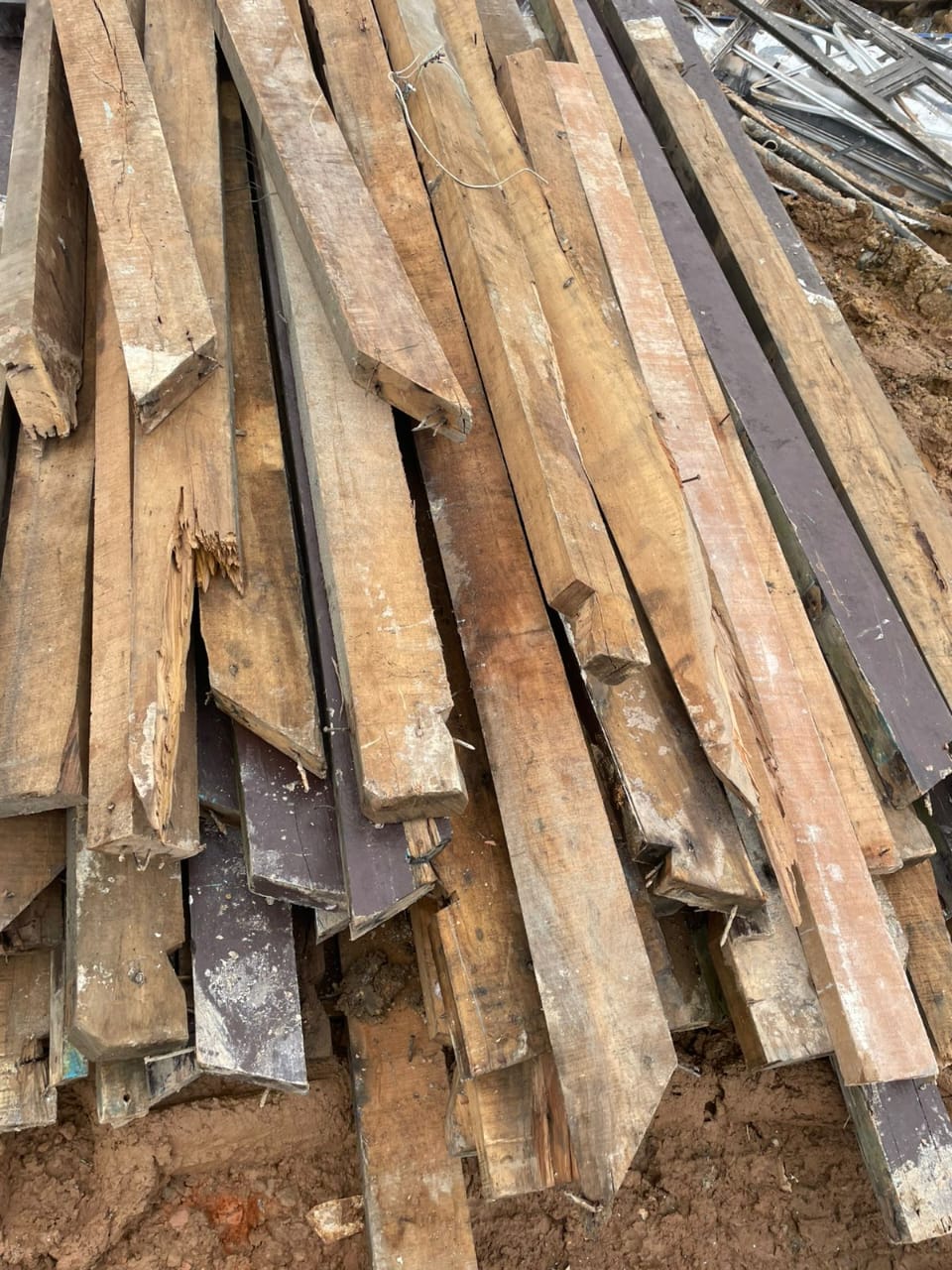 Pilha de pranchas e vigas de madeira reaproveitada de demolição, pronta para revenda e reutilização em novas obras.